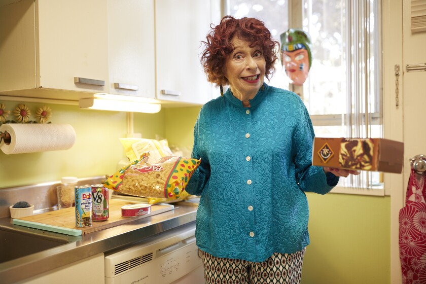 Actor Annie Korzen in her kitchen holding a bag of noodles and a tissue box.