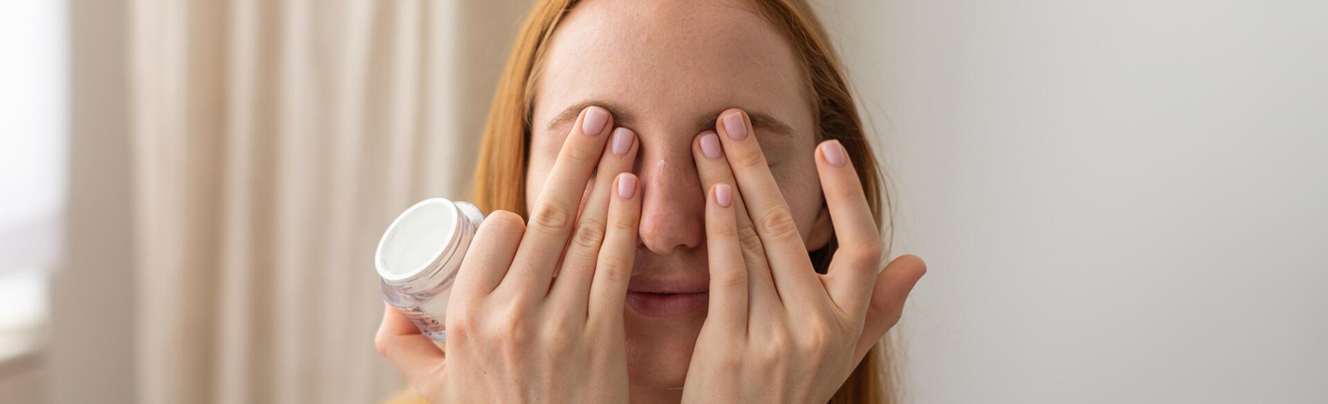 woman putting eye cream over her eyes at home