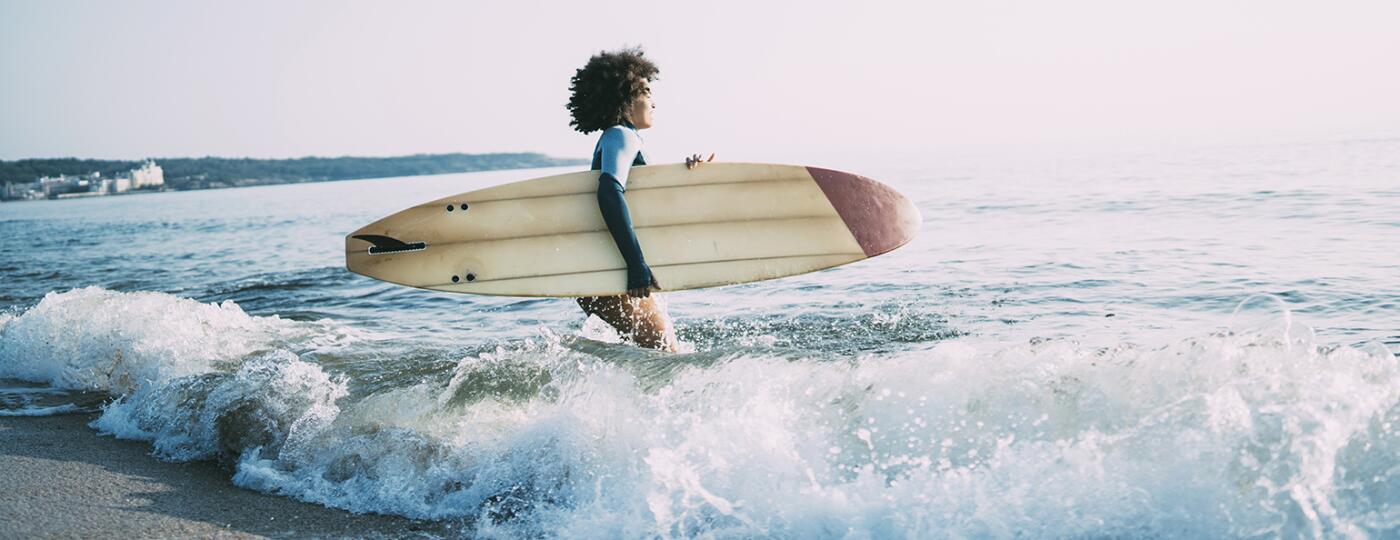 photo_of_african_american_woman_walking_in_ocean_with_surfboard_Surfing_GettyImages-1013089202_1540