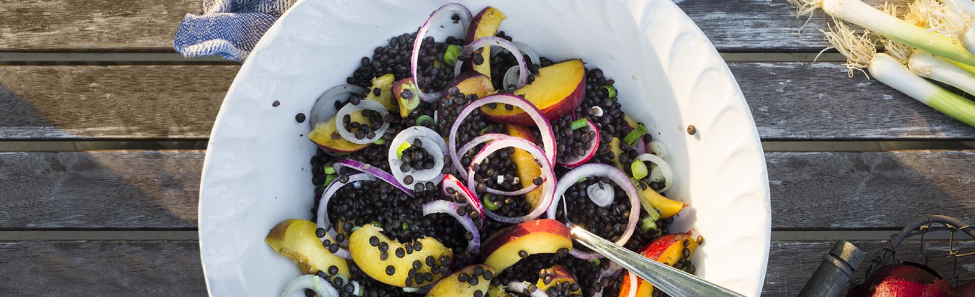 Bowl with lentil and fruit salad on a wooden garden table with kitchen towel