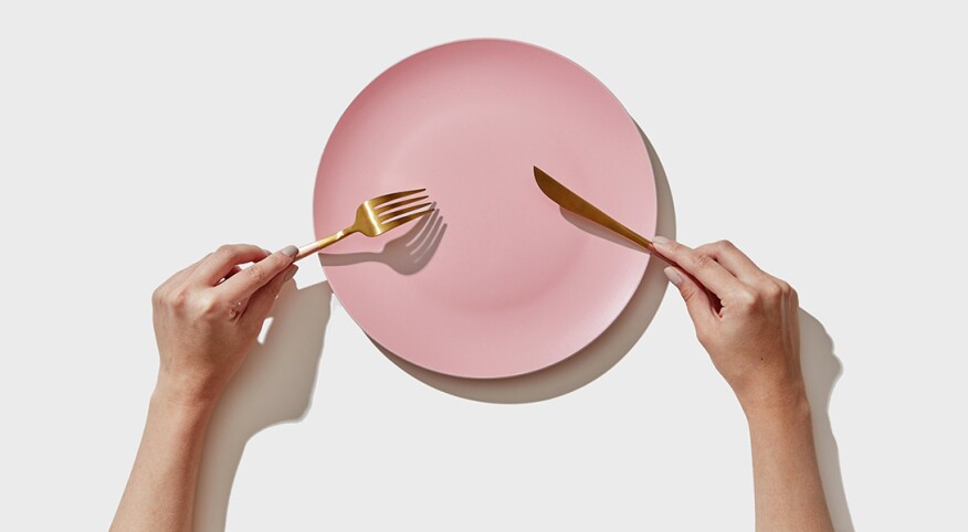 An image of a person holding a fork and knife over an empty plate.