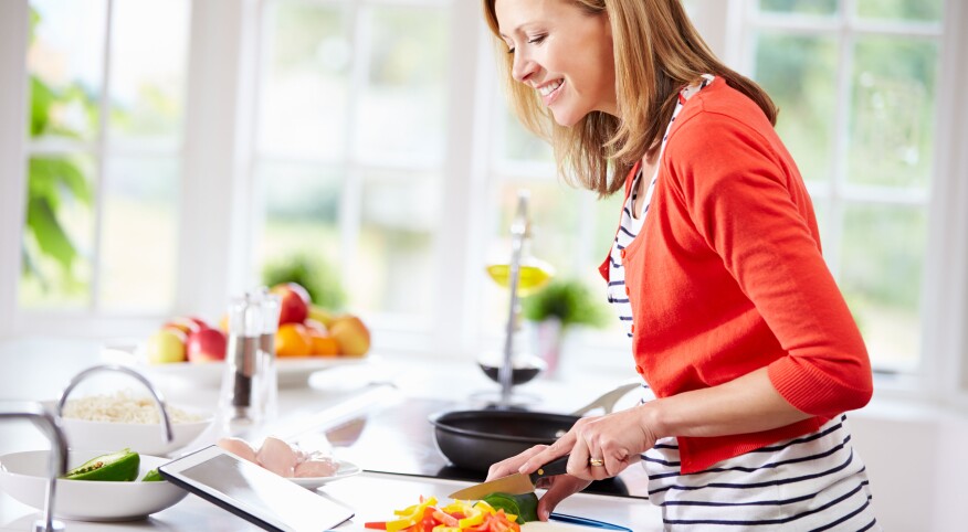 Woman In Kitchen Following Recipe On Digital Tablet