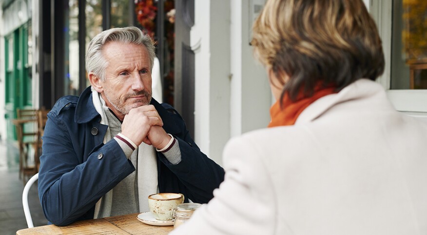 man looking at a woman he's sitting with outside of a cafe