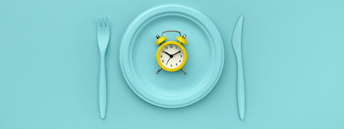 Intermittent fasting, lunch time. Yellow alarm clock, plate and cutlery. Blue background. Minimalistic concept