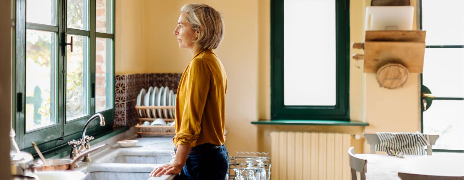 Woman standing in a kitchen at the sink looking out a window