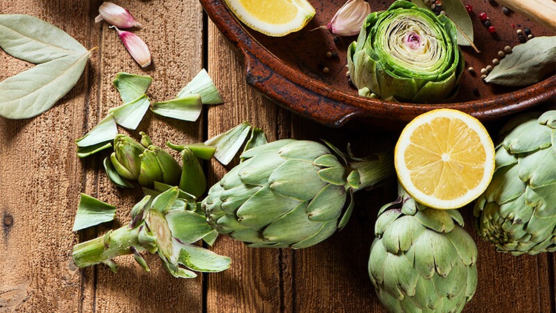 A close-up view of raw artichokes with olive oil and spices on a wooden background