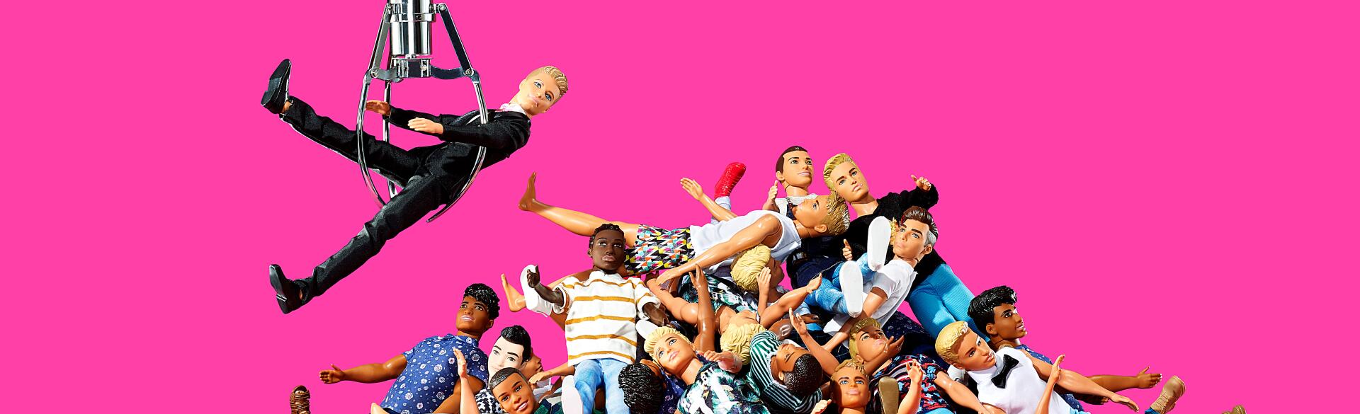 A pile of ken dolls with one ken doll being pulled from the pile by an arcade game claw.