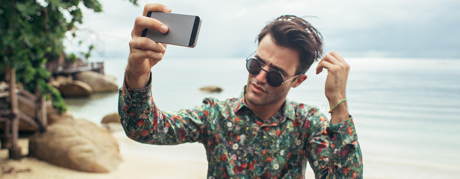 Narcissistic man taking photo of himself on the beach with his phone.