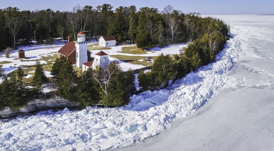 Icy shoreline of Door County Wisconsin with lighthouse, aerial view.