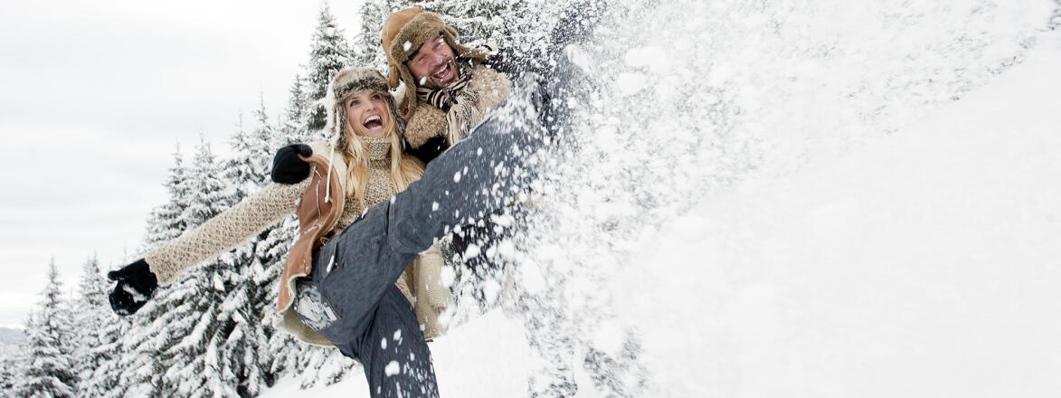 Couple splashing snow in snowy landscape, smiling