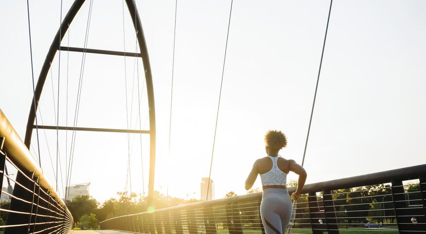 A photo of a woman running down a bridge at sunrise.