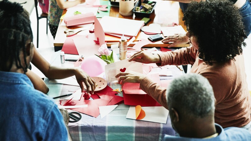 Family and friends gathered around table in home making Valentines Day cards