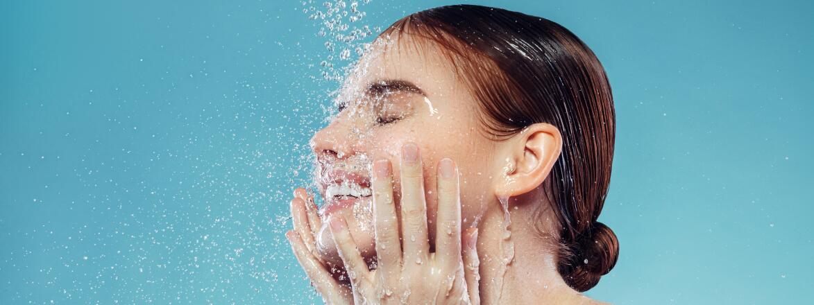 Woman washes her face in front of a blue background
