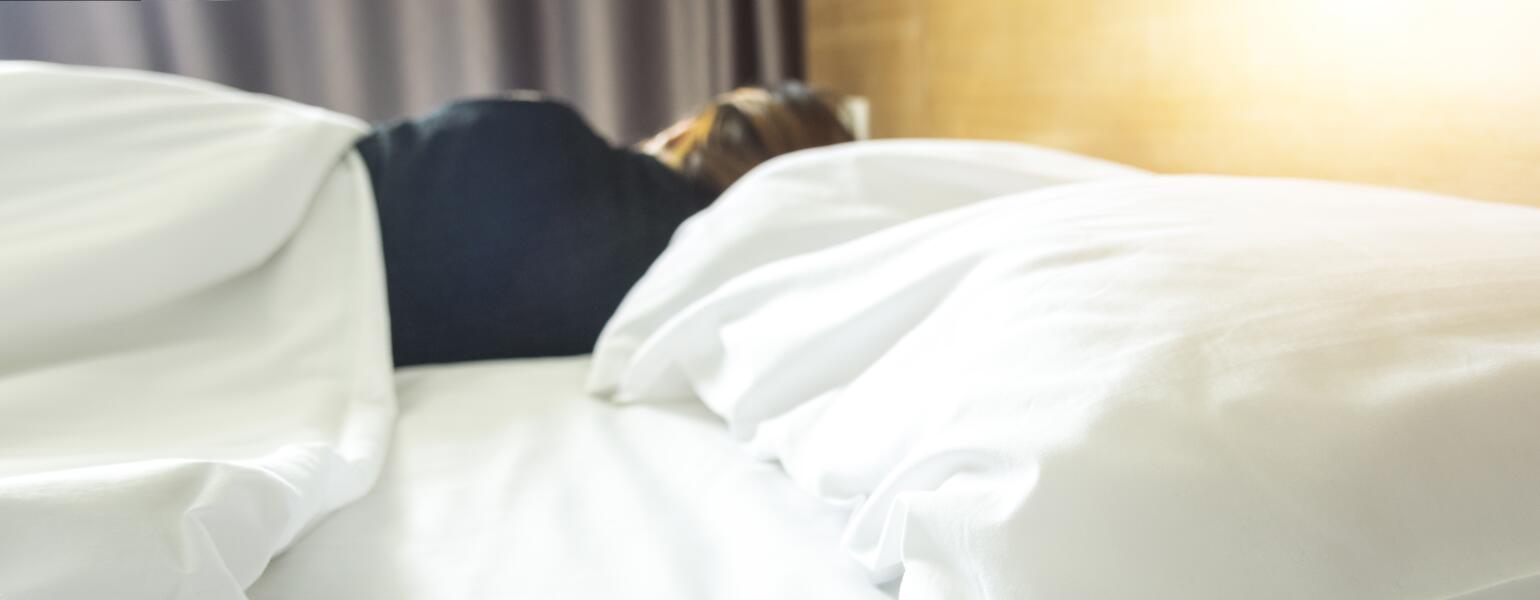 Woman sleeping on the far side of a bed with an empty pillow
