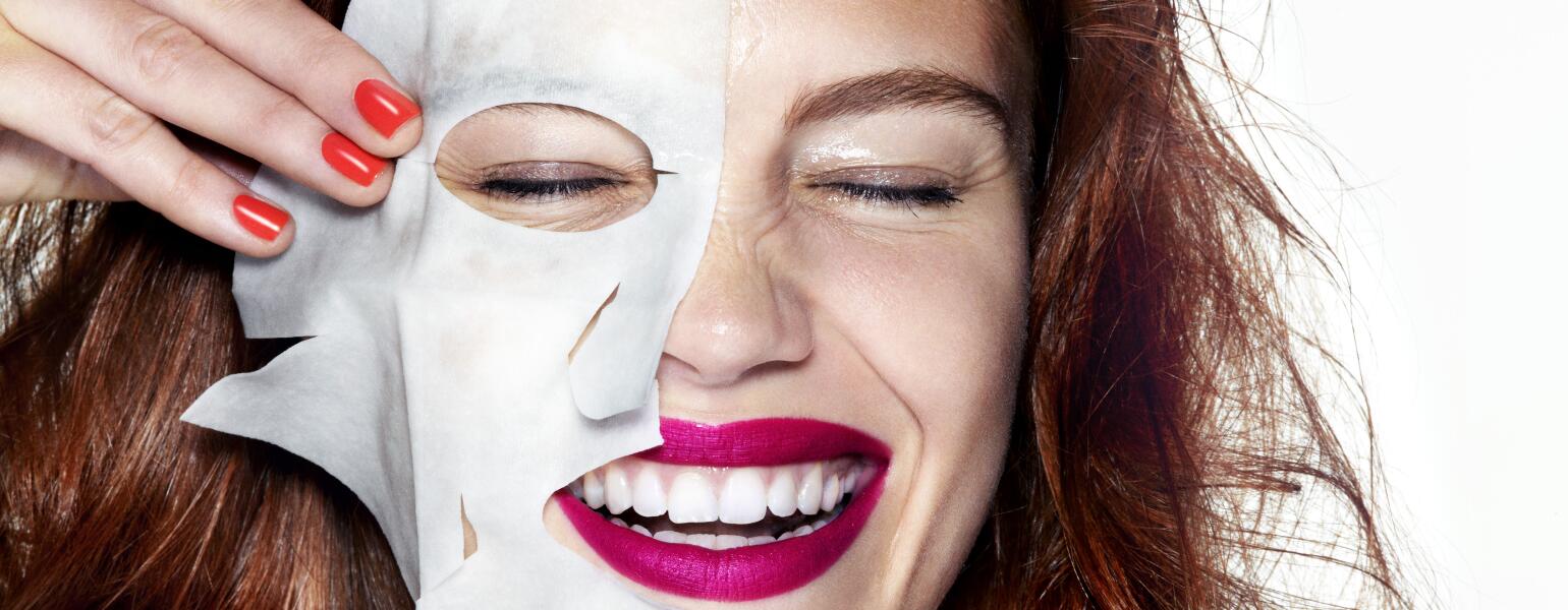 woman smiling with half of a sheet mask on her face