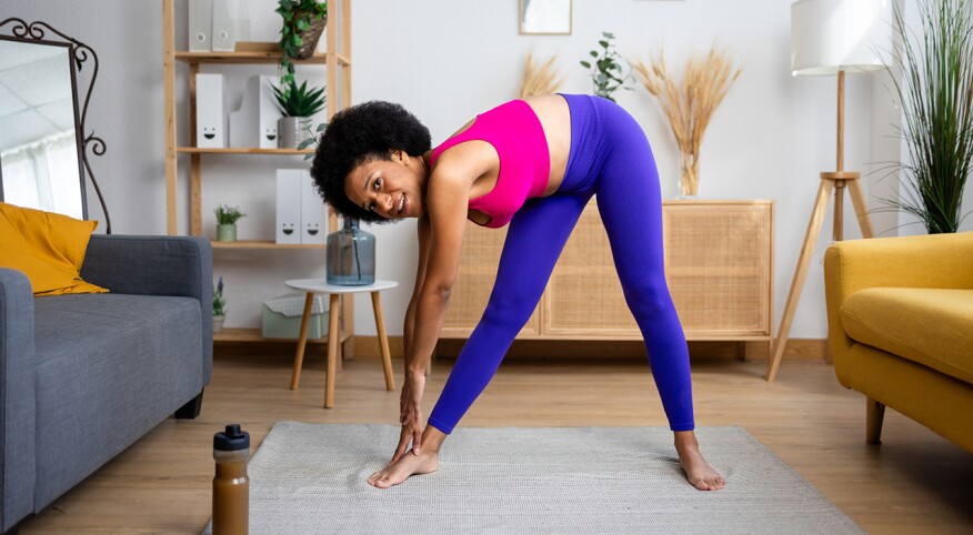 Woman at home bending down to her toes in bright workout clothes