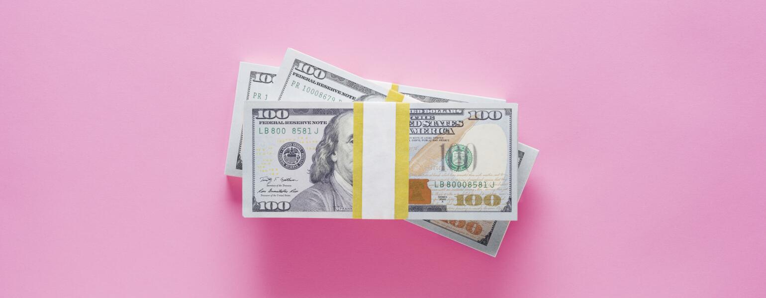 stacks of 100 dollar bills on pink background
