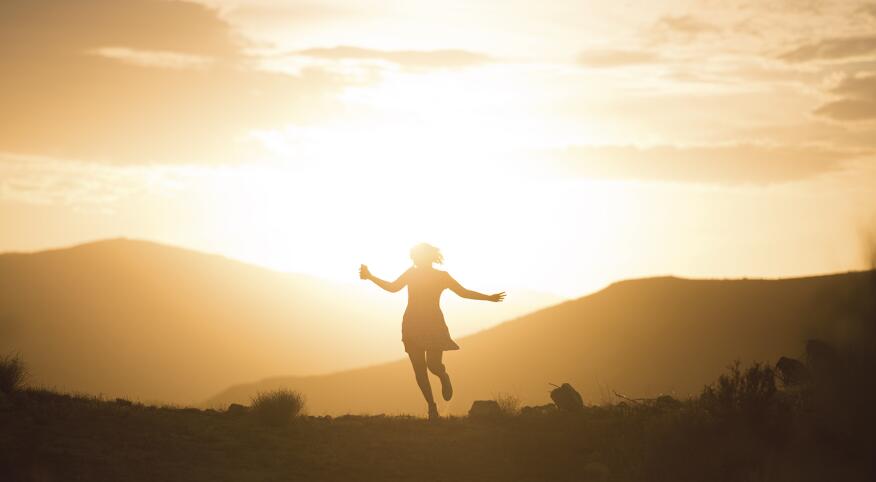 An image of a woman running carefree in the sunrise.