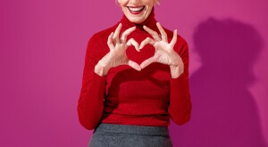 Beautiful mature woman shows heart symbol, shapes love sign with hands