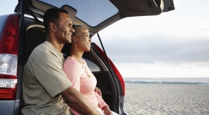 Black couple sitting on hatchback enjoying the beach