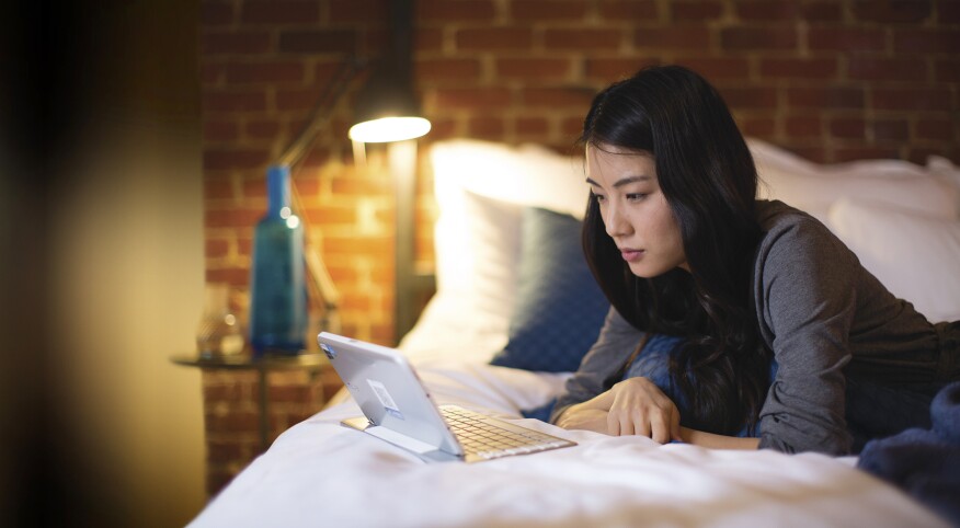 Woman lying on her bed looking at Google on her computer