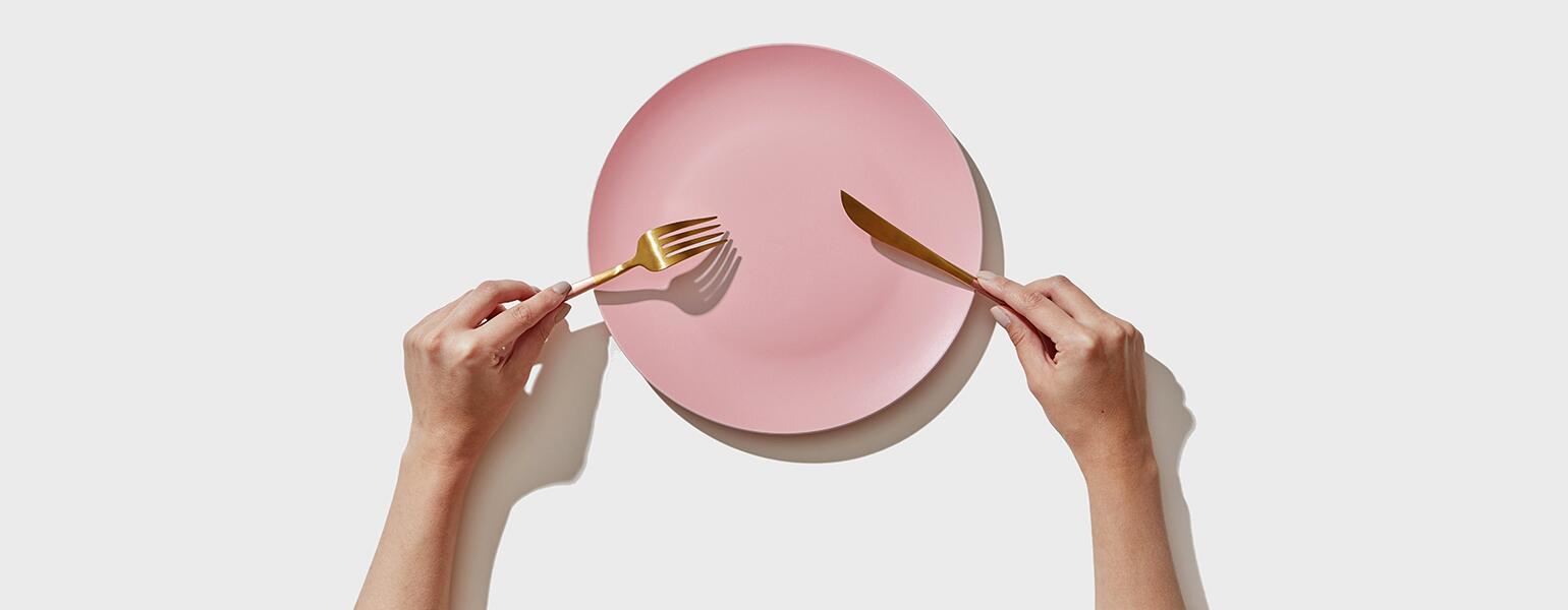 An image of a person holding a fork and knife over an empty plate.
