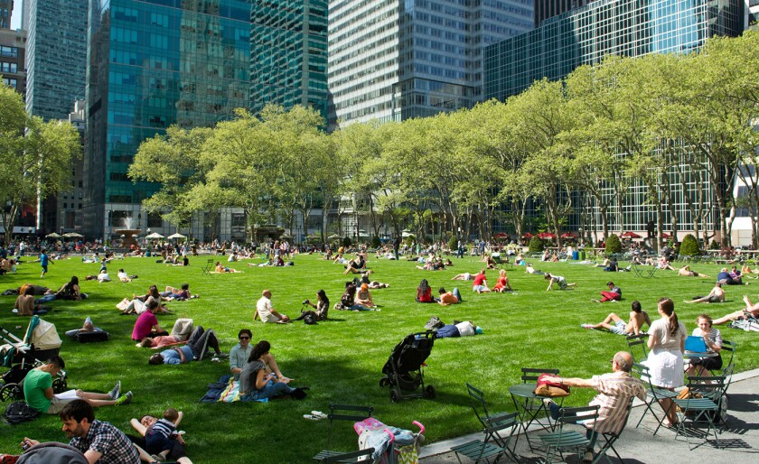 People sprinkled through out Bryant Park in New York City with high rise buildings in the background