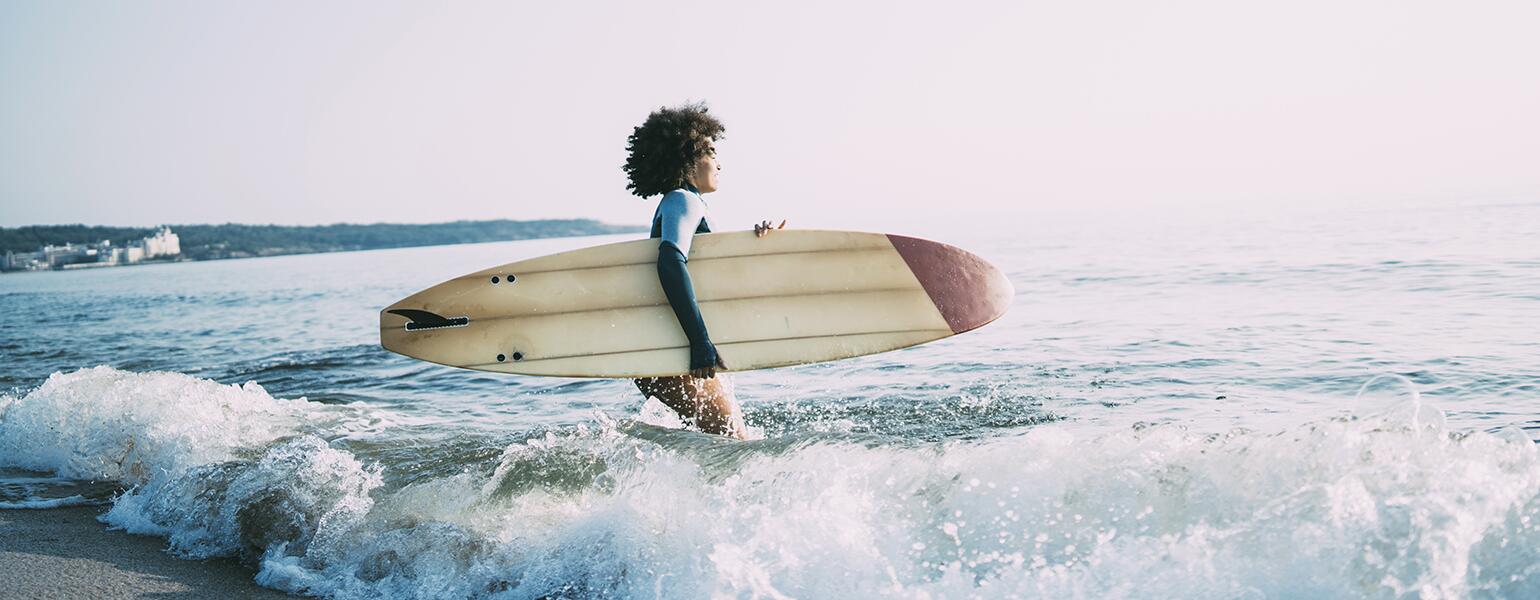 photo_of_african_american_woman_walking_in_ocean_with_surfboard_Surfing_GettyImages-1013089202_1540