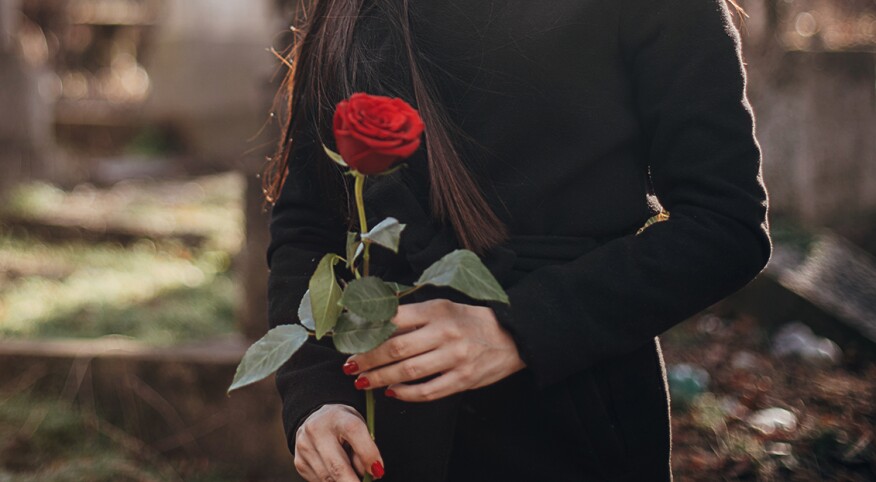 Woman in black carrying a single rose to a funeral