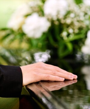 Woman's hand on casket with flowers in the background