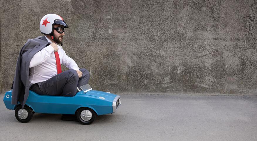 Man wearing a suit and helmet, driving tiny car