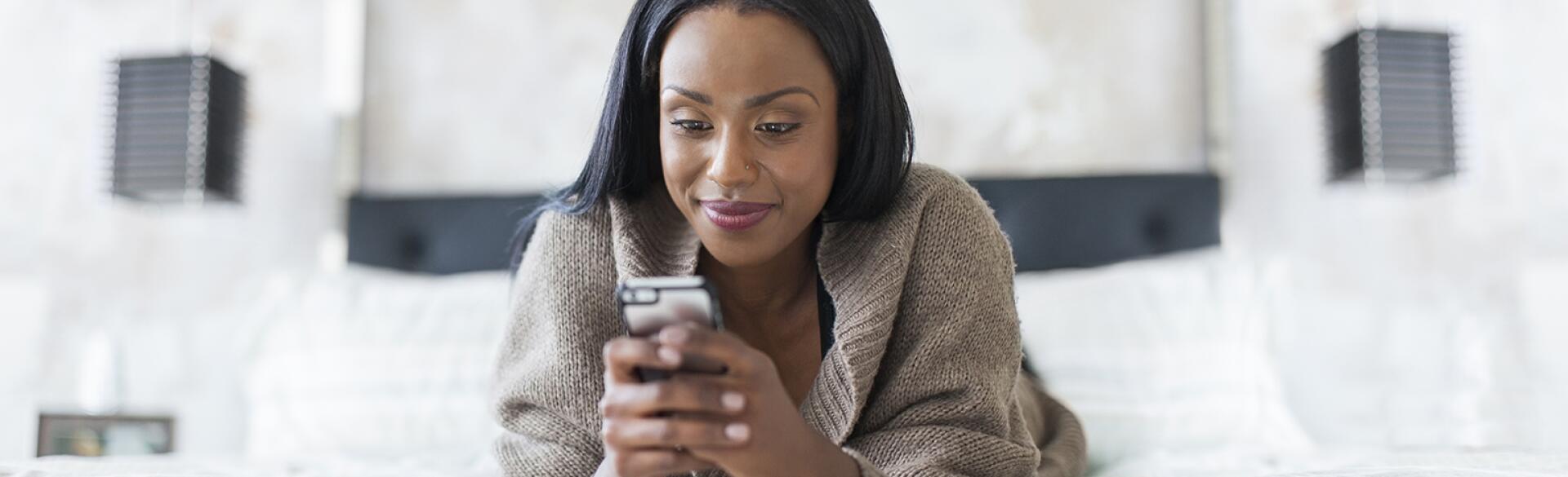A picture of a woman texting on her cellphone while lying in bed.