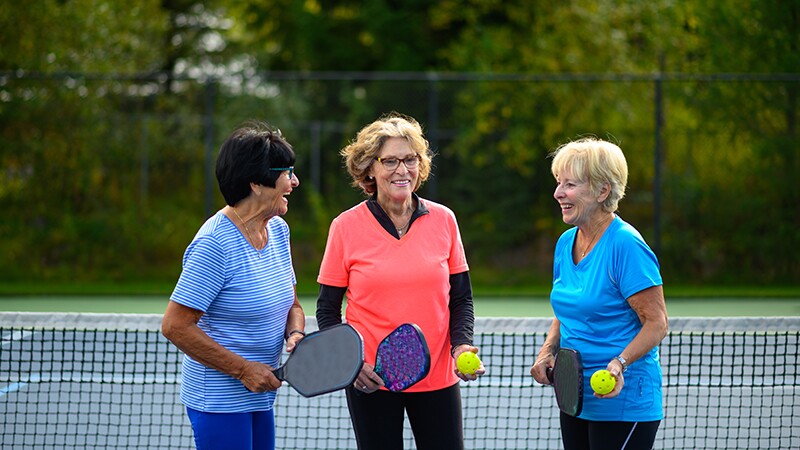 Three women standing together on a pickleball court