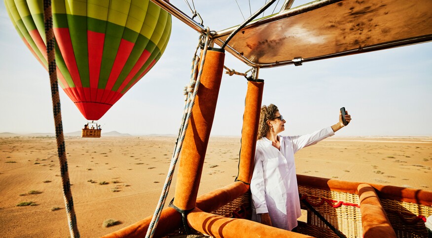 Wide shot of a woman taking a selfie during sunrise hot air balloon ride