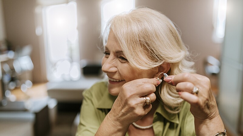 A smiling woman putting a hearing aid in her ear
