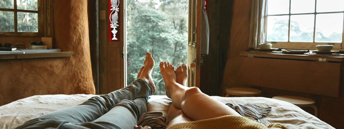 An image of a man and women's legs in bed, where they are lounging together and holding hands.