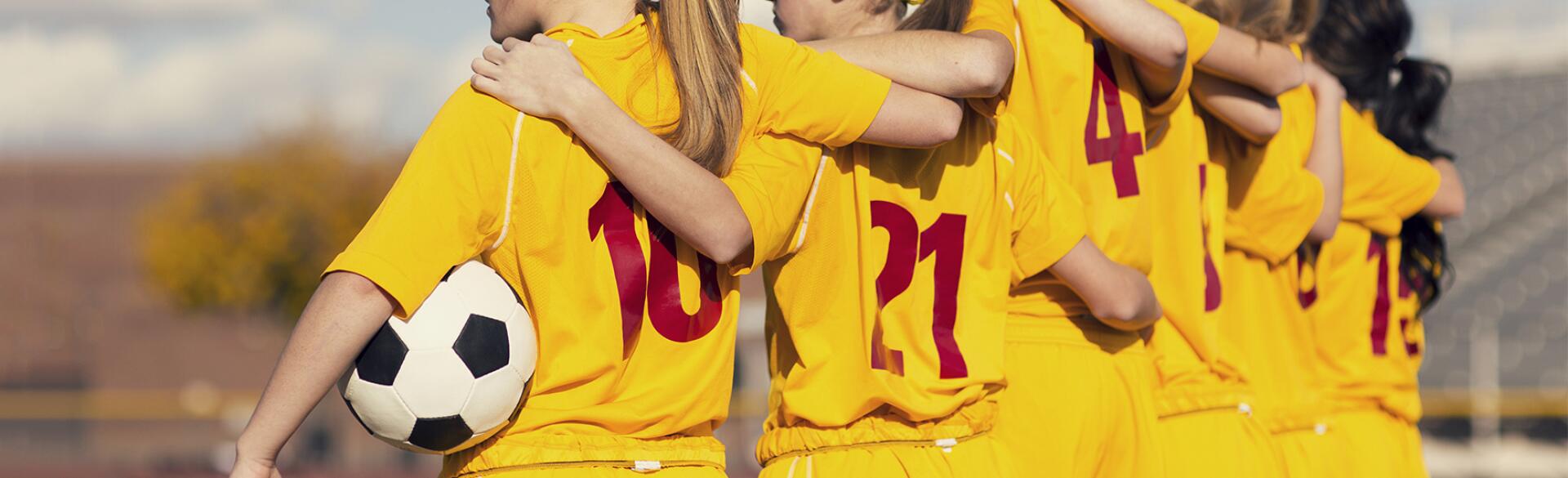 Young girls playing soccer standing on the sidelines arm and arm before the game