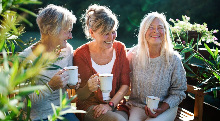 Three middle-aged women on bench with coffee, talking and laughing