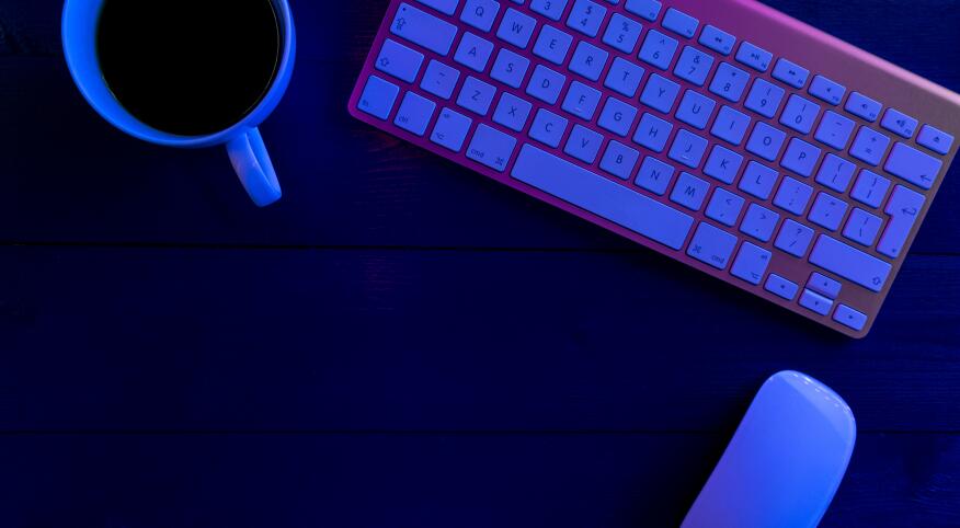 cup of coffee keyboard and computer mouse on desk in moody blue light