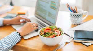 Woman typing on laptop eating a salad