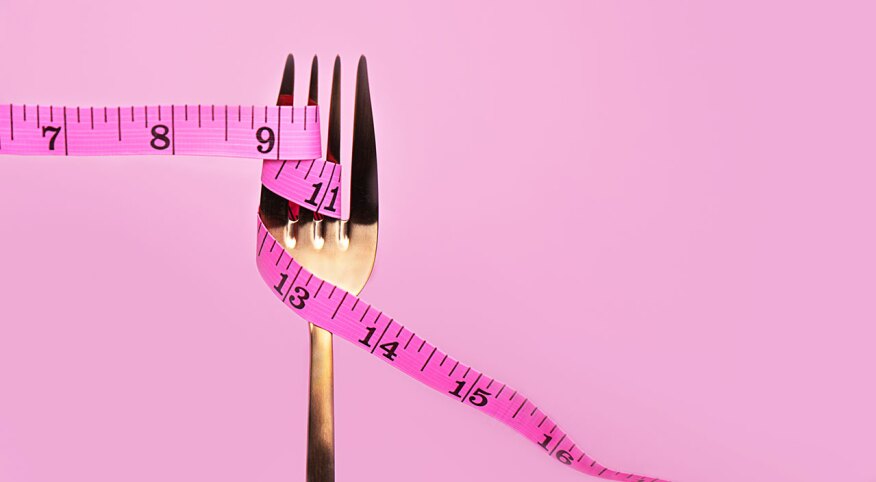 Pink measuring tape and fork on pink background.
