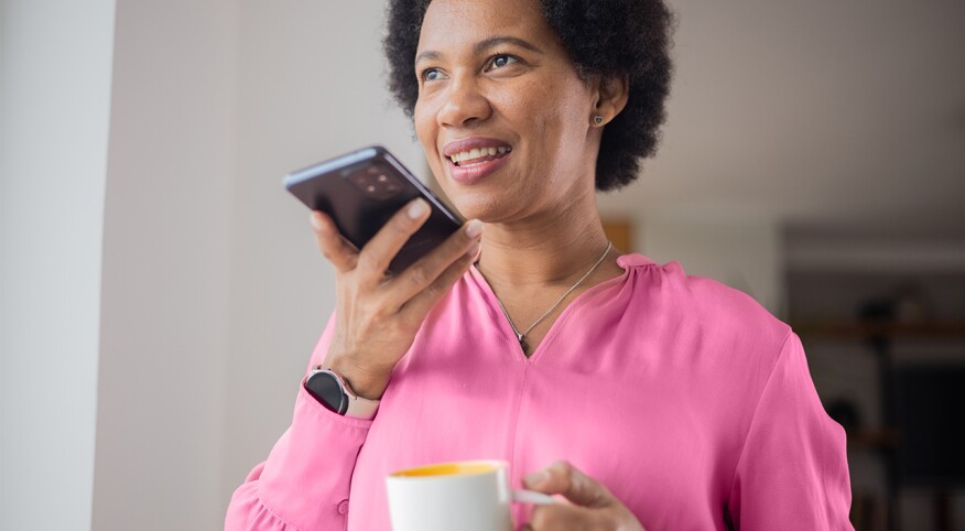 woman drinking tea and audio journaling on cell phone