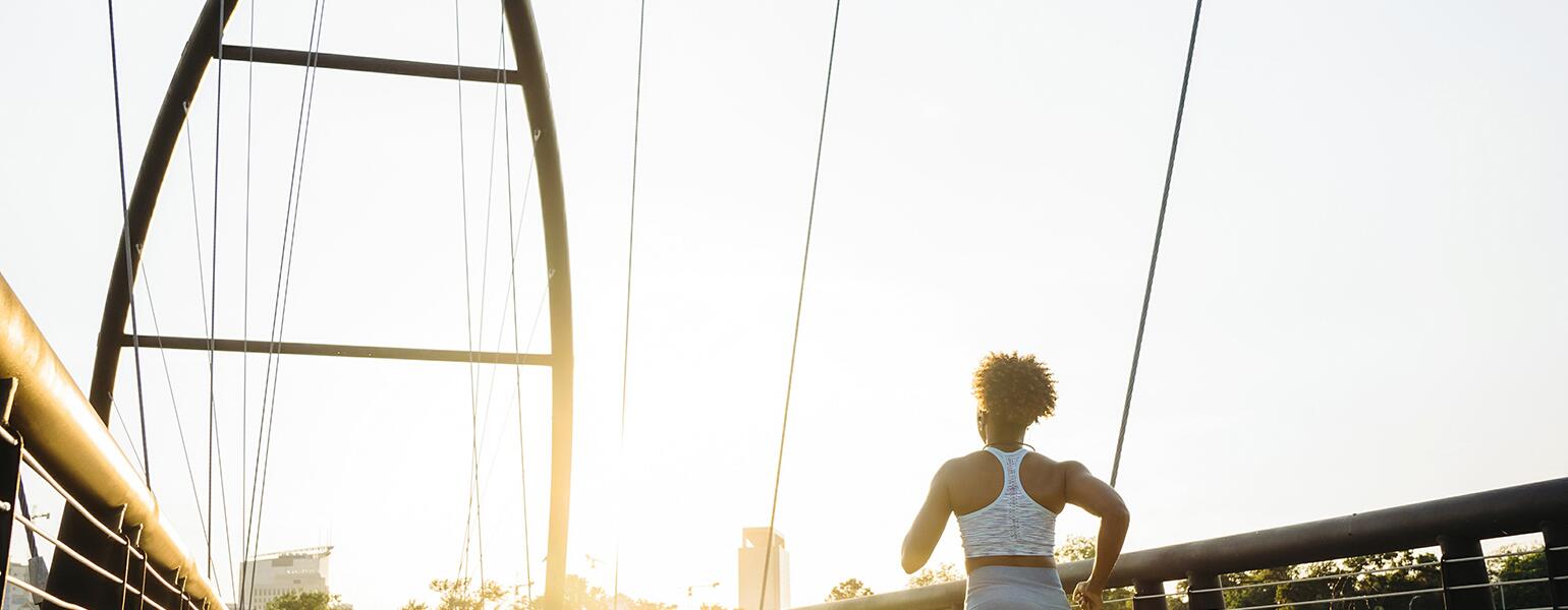 A photo of a woman running down a bridge at sunrise.