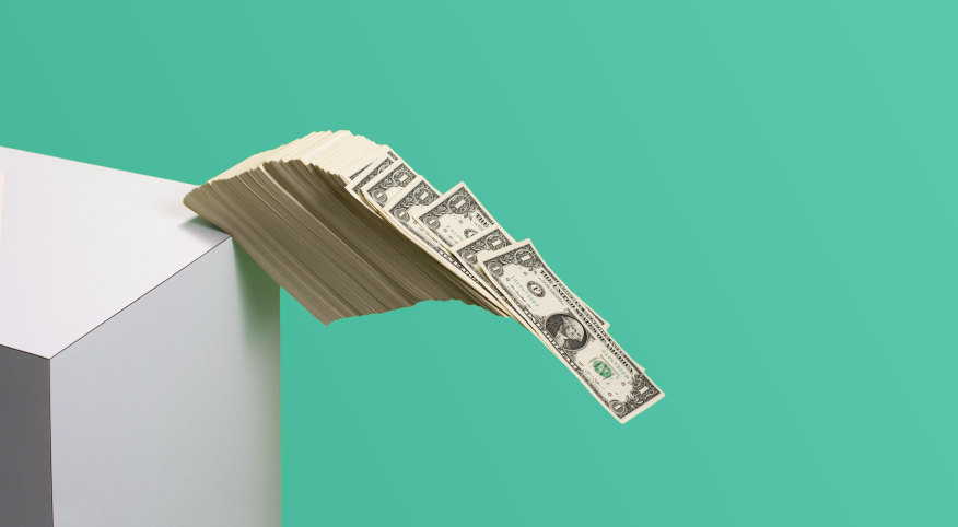 Stack of dollar bills falling of the edge of a shelf on a green background