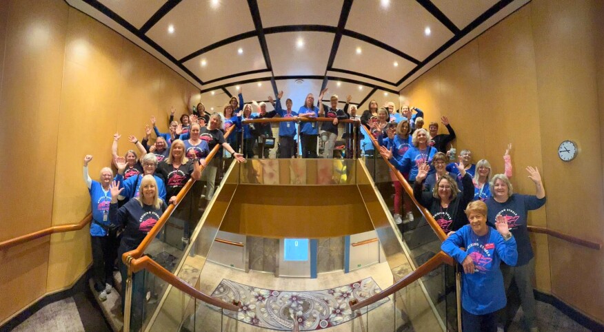 A group of numerous women sanding and waving from the stairs of a cruise