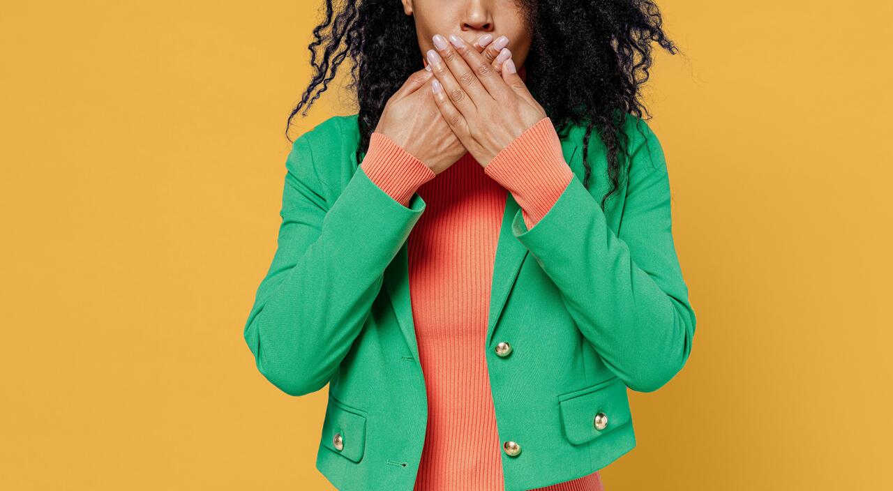 Surprised woman covering her mouth with hands on a bright yellow background