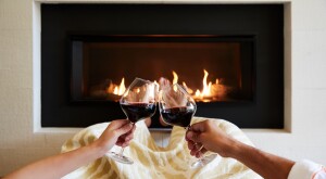 Couple with two glasses of red wine in front of a fireplace.