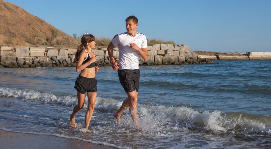Father and daughter running along the seashore.