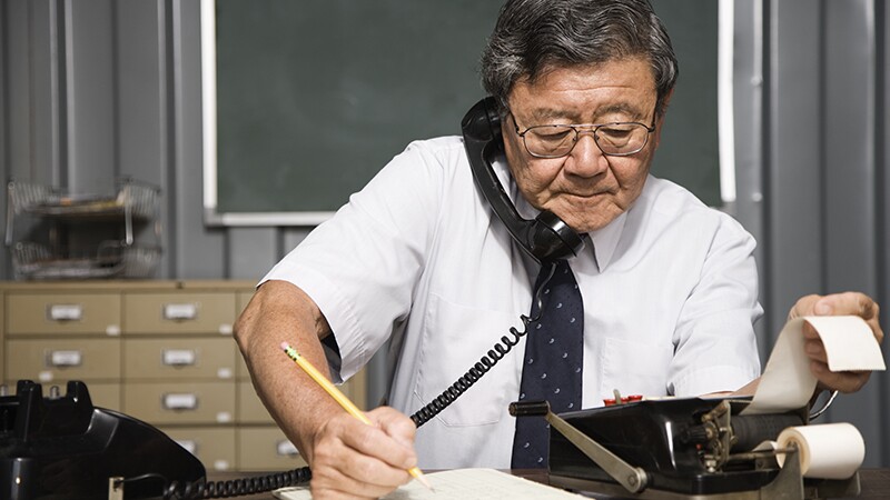A man using a phone and adding machine while writing all at the same time