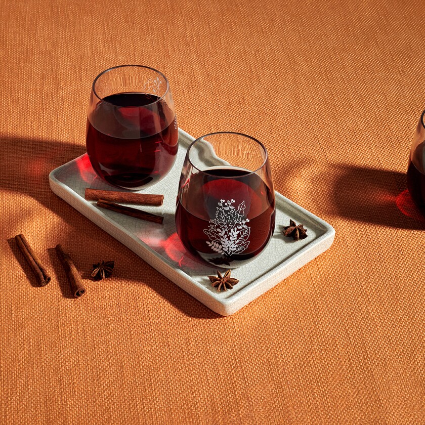 2 wine tumblers filled with red wine next to cinnamon sticks on a white tray
